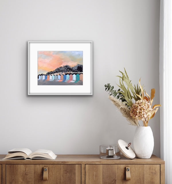 Framed artwork on a wall above a wooden cabinet with decorative items.