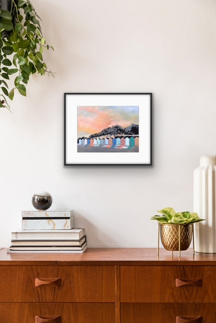 Framed artwork on a wall above a wooden cabinet with decorative items.