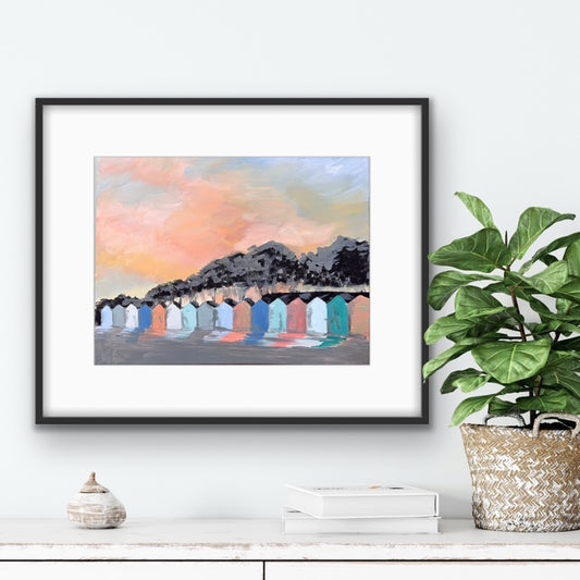 Framed artwork of colorful beach huts with a plant and decor items on a shelf below.